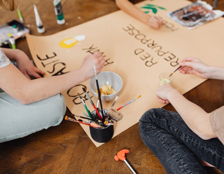 Artists working together on a large canvas with paintbrushes and bowls, featuring hand-painted words like 'Repurpose' and 'Waste,' highlighting NaksheZeast’s commitment to sustainable art.