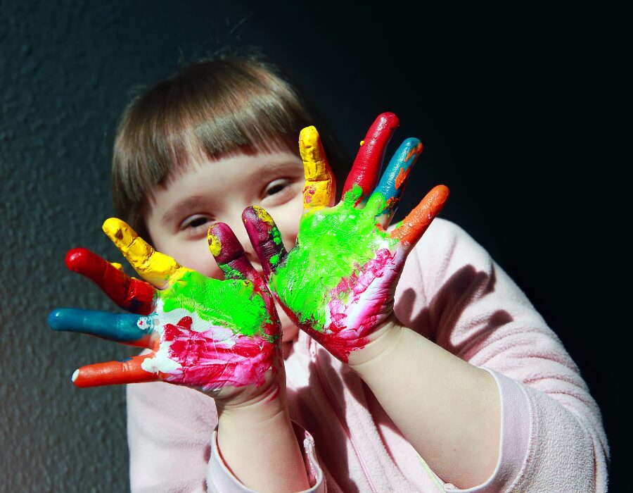 Close-up of a smiling young girl with paint-covered hands in bright shades of green, red, and yellow, capturing the creative joy at NaksheZeast.