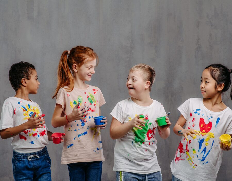 A group of cheerful children with diverse abilities smiling and laughing together while covered in colorful finger paint, representing the inclusive spirit of NaksheZeast.